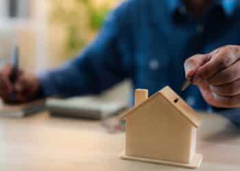 A man hand putting coins into a house bank saving bank for account save money. Planning step up, saving money for future plan, retirement fund. A business investment-finance accounting concept.